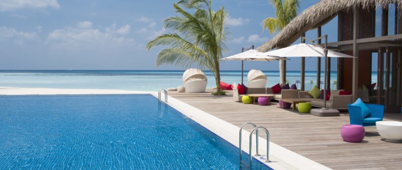 Club Med Kani, aux Maldives - Vue en biais de la seule piscine extérieure avec palmiers et chaises longues.