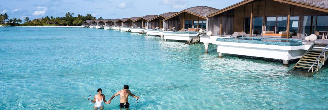 Club Med Villas de FInolhu, aux Maldives - Un couple se baignant dans la lagune devant une villa